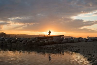 Man standing on rock by sea against sky during sunset