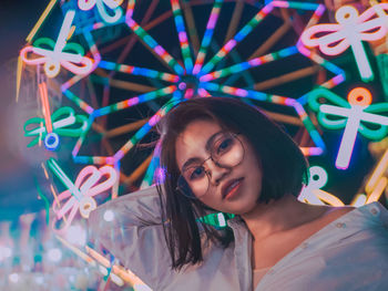 Portrait of smiling young woman against illuminated ferris wheel