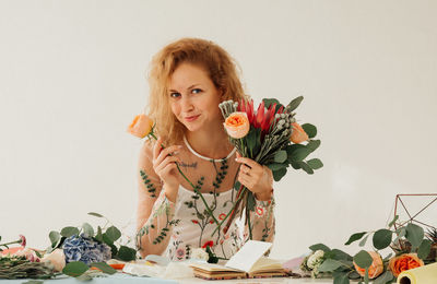 Portrait of smiling young woman holding plant against white background