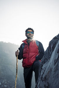 Young traveler in red snow jacket and a backpack standing on blue isolated background. 