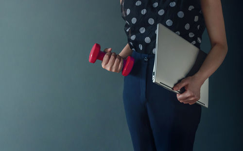 Midsection of woman holding camera while standing against gray background