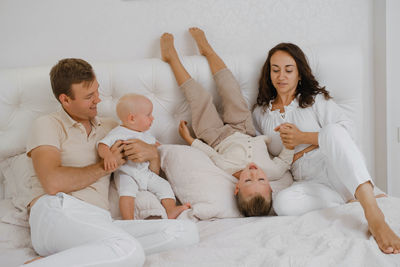 Family with two kids on the bed having fun. mather, father baby and toddler sons are happy 