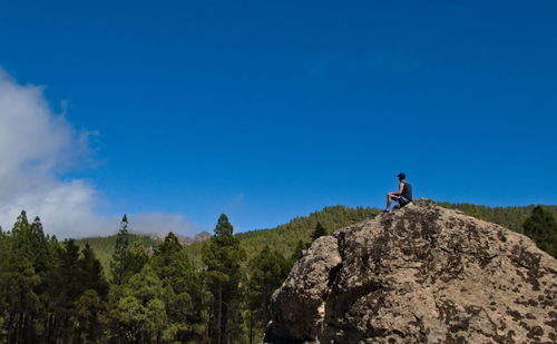 Man on rock against blue sky