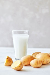 Potato milk in a glass mug stands on the table next to fresh potato tubers. alternative plant milk