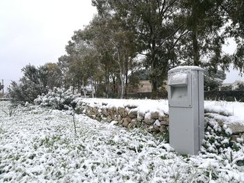 Snow covered land by trees on field against sky