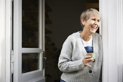 Happy mature woman having coffee at entrance of art studio