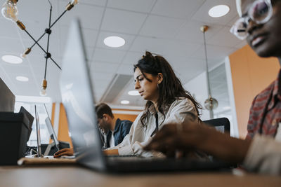 Young businesswoman using laptop while working amidst colleagues at desk in creative office