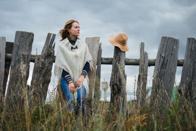 Rear view of woman standing on wooden post against cloudy sky