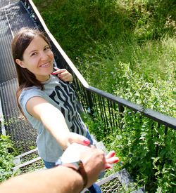 Portrait of happy woman holding cropped hand in park during sunny day