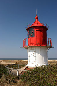 Lighthouse by sea against clear sky