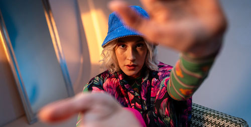 A woman wearing a blue hat and a colorful jacket is sitting on a couch