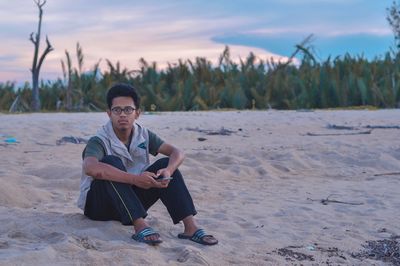 Young man sitting on beach against sky