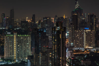 Illuminated modern buildings in city against sky at night