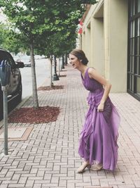 Cheerful young woman wearing purple dress standing on footpath