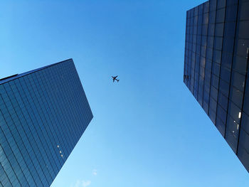Commercial airplane crossing the sky between two modern office buildings.