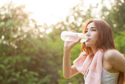 Woman drinking water from bottle against trees