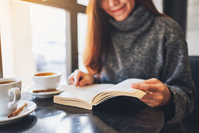 Woman reading book while having coffee at table