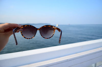 Cropped hand of woman holding sunglasses against sea