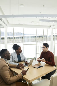 Young businessman discussing with colleagues sitting at desk in office