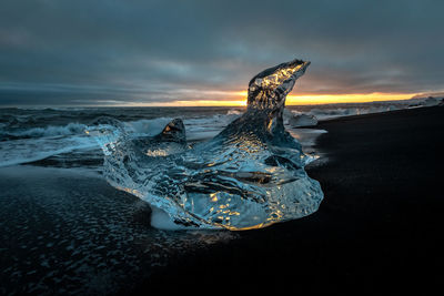 Ice at beach against cloudy sky during sunset