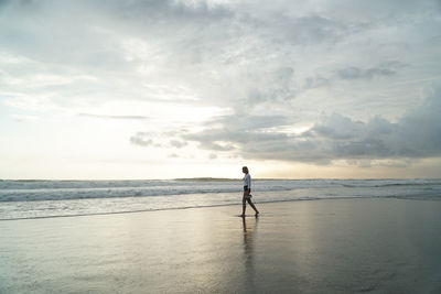 Woman walking at beach against sky during sunset