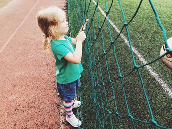 Side view of girl standing by net in playground