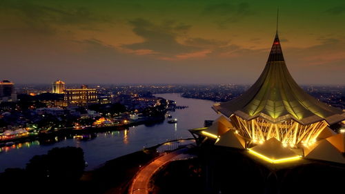 Illuminated sarawak state legislative assembly building by river at dusk