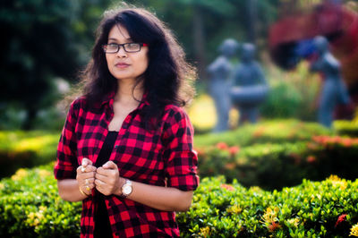 Portrait of beautiful young woman standing against plants