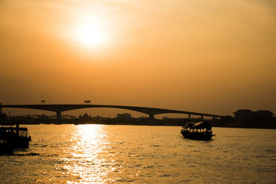 Silhouette bridge over river against sky during sunset