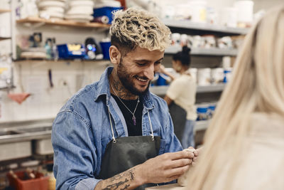 Smiling young man with blond hair molding clay in art class