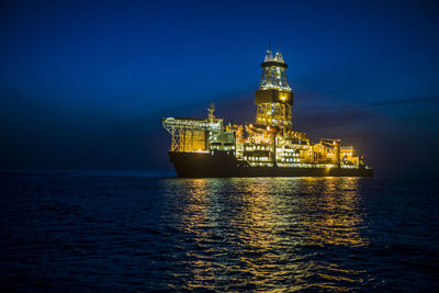 Illuminated drill ship on sea against sky at night