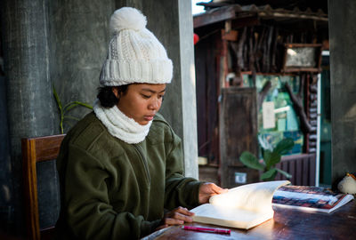 Concept of a female student in winter coat sitting alone reading a book on the balcony