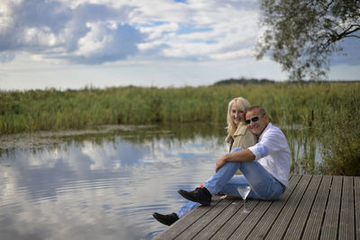 Portrait of couple sitting on pier over lake