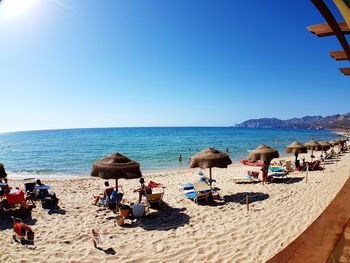 People on beach against clear blue sky