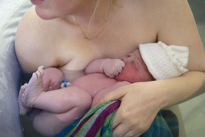 Midsection of mother holding baby while sitting in bathtub