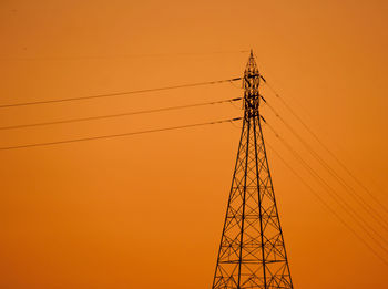 Low angle view of electricity pylon against orange sky