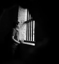 Side view of young woman looking through window at home