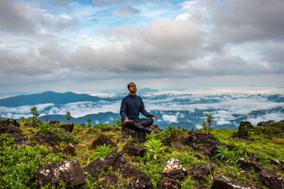 Man sitting on rock against sky