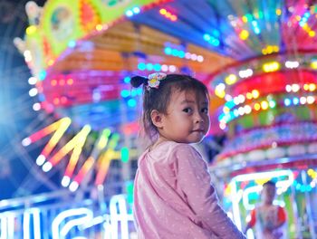 Cute boy looking at illuminated carousel in amusement park