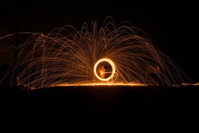 Person spinning wire wools while standing on field against sky at night