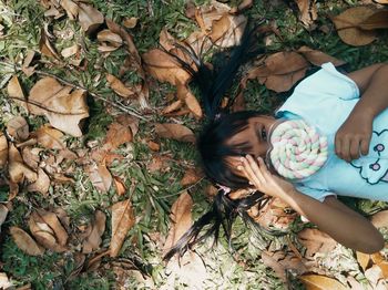 High angle portrait of girl holding lollipop while lying on land