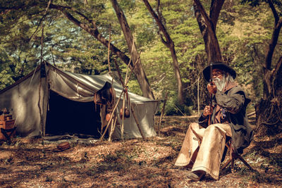 Woman sitting on field by trees in forest