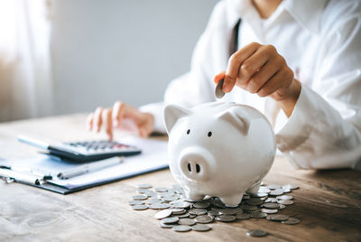 Midsection of woman inserting coin in piggy bank on table