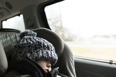 Toddler wearing winter hat sleeps while in carseat inside minivan