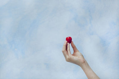 Cropped hand holding cherry against sky