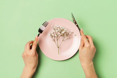 Cropped hand of woman holding eating utensil over plate against green background