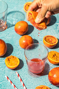 From above hand of crop anonymous person squeezing juice from blood orange into glass placed on table in light room person