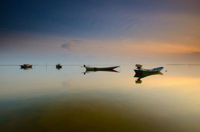 Silhouette boats moored in lake against sky during sunset