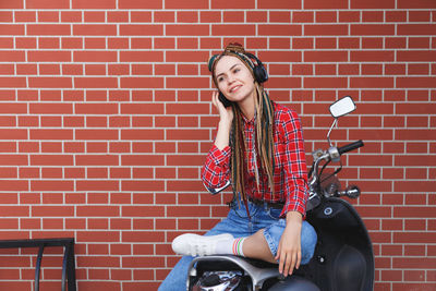 Full length of woman sitting against brick wall