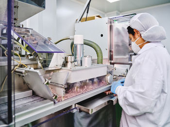 Side view of female factory worker in uniform operating conveyor with pills in pharmaceutical manufacturing laboratory